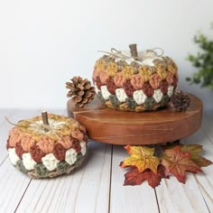 two crocheted pumpkins sitting on top of a wooden stand next to leaves