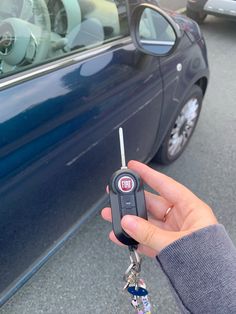 a hand holding a car key in front of a blue car