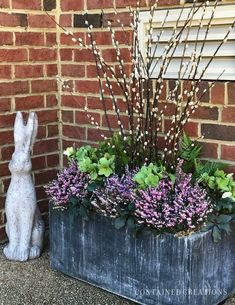 a planter filled with purple flowers next to a white rabbit statue and brick wall