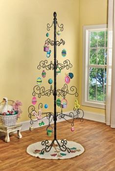 a black metal christmas tree with lots of ornaments on it's stand in front of a window