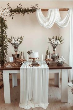 a table topped with cake and flowers on top of a wooden table covered in white drapes