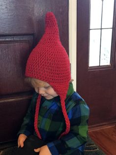 a little boy sitting on the floor wearing a red knitted hat