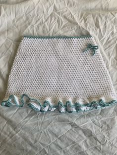 a white crocheted purse with green trim on top of a bed covered in sheets