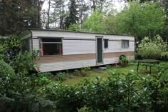 an old mobile home in the middle of a wooded area with trees and bushes around it