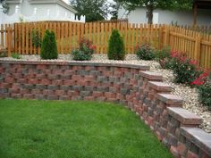 a brick retaining wall in the middle of a yard with flowers and shrubs around it