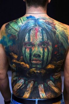 the back of a man's body with tattoos on it and his face painted in different colors