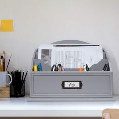 an office desk with a gray file box on it and pens, pencils, and other office supplies