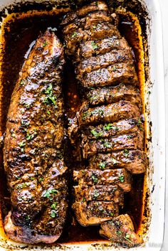 two steaks in a casserole dish with sauce and parsley