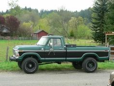 a green and black truck parked in front of a fenced in area with trees