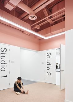 a woman sitting on the floor in an empty room with two doors and pink walls