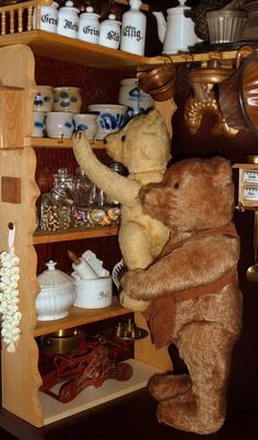 two brown teddy bears standing on their hind legs in a shelf filled with teapots