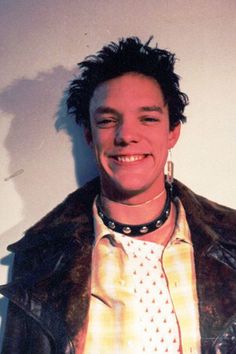 a young man wearing a leather jacket and tie smiles at the camera while standing in front of a white wall