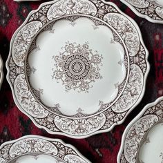 several white and brown plates sitting on top of a red tablecloth covered floor next to each other