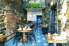 an empty restaurant with tables and chairs in front of a brick wall filled with potted plants