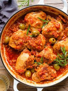 a pan filled with chicken and olives on top of a wooden table