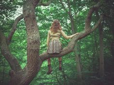 a woman sitting on top of a tree branch