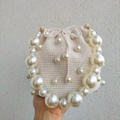 a hand holding a white purse with pearls on it