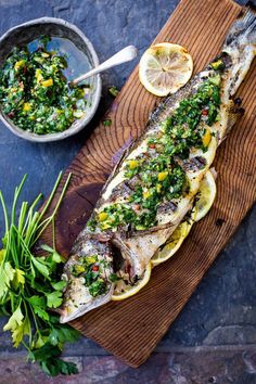 a fish is sitting on a cutting board with lemons and herbs next to it