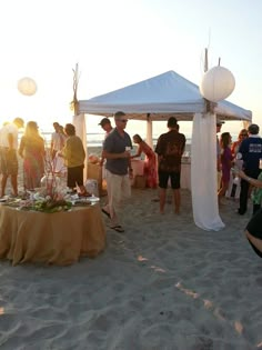 a group of people standing on top of a sandy beach next to a white tent