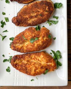 three pieces of breaded chicken on a white plate with parsley sprigs