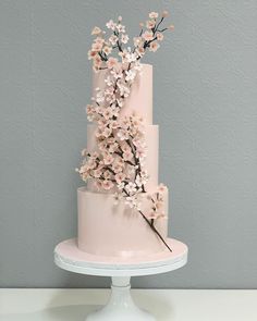 a three tiered cake with pink flowers on the top and bottom, sitting on a white pedestal