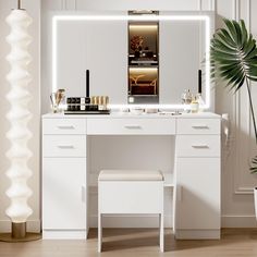 a white vanity with lighted mirror and stool in a room next to a potted plant