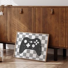 a framed video game controller sitting on the floor next to a wooden cabinet with drawers