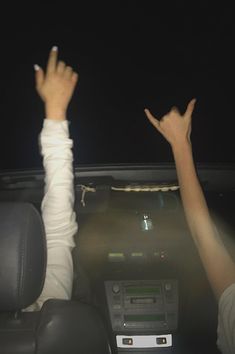 two people sitting in a car with their hands up