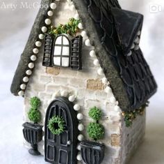 a small white house with black shutters and green plants on the front window sill