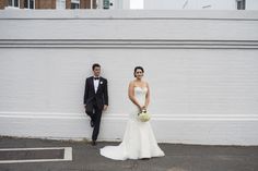 a bride and groom standing in front of a white wall