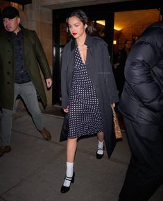 a woman in a polka dot dress and trench coat is walking down the street with her hand on her hip