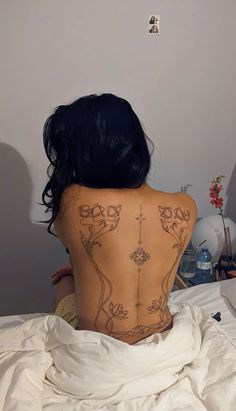 a woman with tattoos on her back sitting in bed