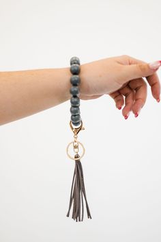 a woman's hand holding onto a beaded bracelet with a tasseled charm