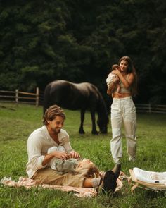 a man holding a baby while sitting on top of a blanket next to a horse