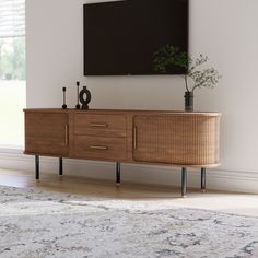 a wooden sideboard with two plants on it in front of a large screen mounted to the wall