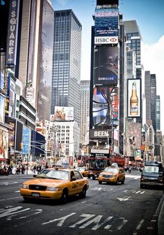 taxi cabs and taxis driving down a busy city street with tall buildings in the background