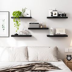 a bed with white sheets and black shelves on the wall above it, along with other items