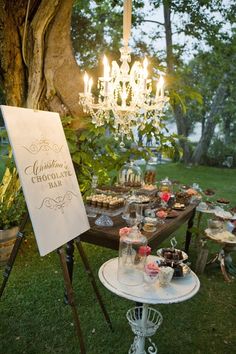 an outdoor dessert table with cupcakes and pastries under a chandelier