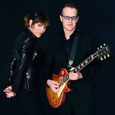 two people standing next to each other holding guitars