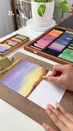 a person is painting with crayons on paper and watercolors in front of them