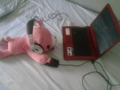 a pink teddy bear laying next to a laptop computer on a bed with headphones