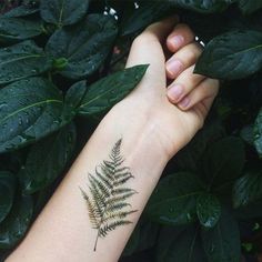 a woman's arm with a fern tattoo on it and green leaves around her wrist