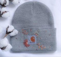 a gray beanie with an orange and white patch on it next to cotton flowers