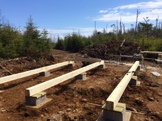 some wooden benches sitting in the middle of a dirt and grass area with trees behind them