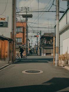 a man riding a bike down a street next to tall buildings and power lines in the background