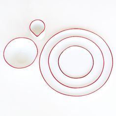 a white plate with red trim around it and two plates on the side, next to each other