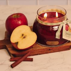 an apple and cinnamon stick sit next to a candle on a cutting board with apples in the background