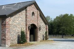 an old brick building with a black metal roof and arched doorways is shown in front of a gravel parking lot