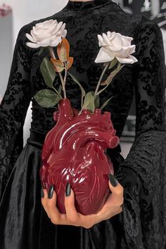 a woman holding a heart shaped vase with flowers in it's hands and wearing a black dress