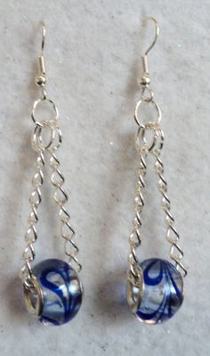 two blue and white glass beads hanging from silver earwires on a marble surface